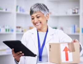 Happy woman, pharmacist and tablet in logistics for inventory inspection or stock at pharmacy. Senior female person in medical or healthcare checking pharmaceutical product or checklist on technology